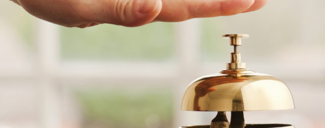 Hand ringing brass bell on hotel reception desk